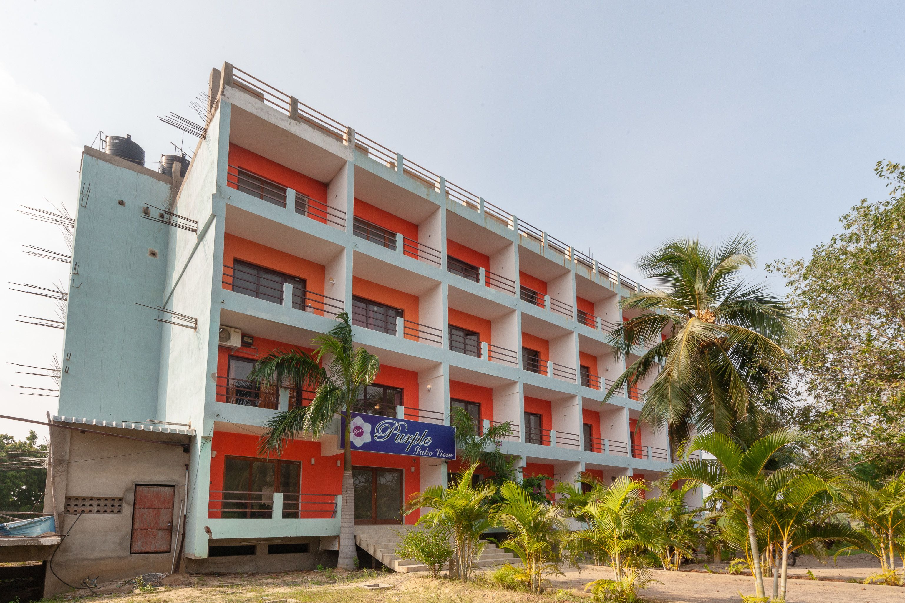 A multi-story building with balconies, a signboard, and palm trees in the foreground.