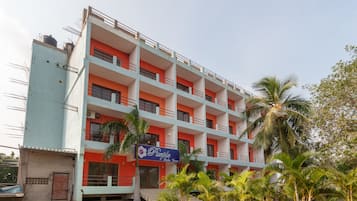 A multi-story building with balconies, a signboard, and palm trees in the foreground.