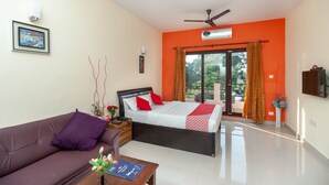 Un dormitorio con cama, sofá, mesita de noche, una mesa con flores y ventana con cortinas.