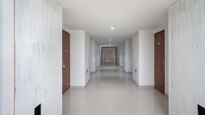 Un pasillo largo y estrecho con paredes blancas y puertas de madera, que conduce a una habitación al final.