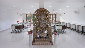 Un comedor con una estatua central, mesas, sillas y plantas en macetas.