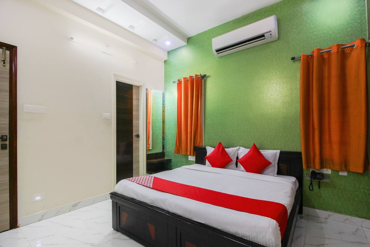 Habitación de hotel con cama, paredes verdes y cortinas naranjas.