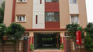 A multi-story building with a central entrance, red and beige color scheme, and a sign indicating room number 6. - OYO 7571 Madhapur (Hyderabad)