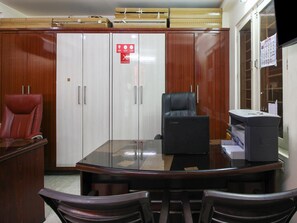Una sala de conferencias con una mesa de vidrio, dos sillas, una silla roja, una silla de oficina negra y un archivador.