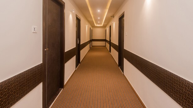 A hotel hallway with a patterned carpet, dark wooden doors, and recessed lighting. - OYO 22039 Hotel Bkc Grand (Mumbai)