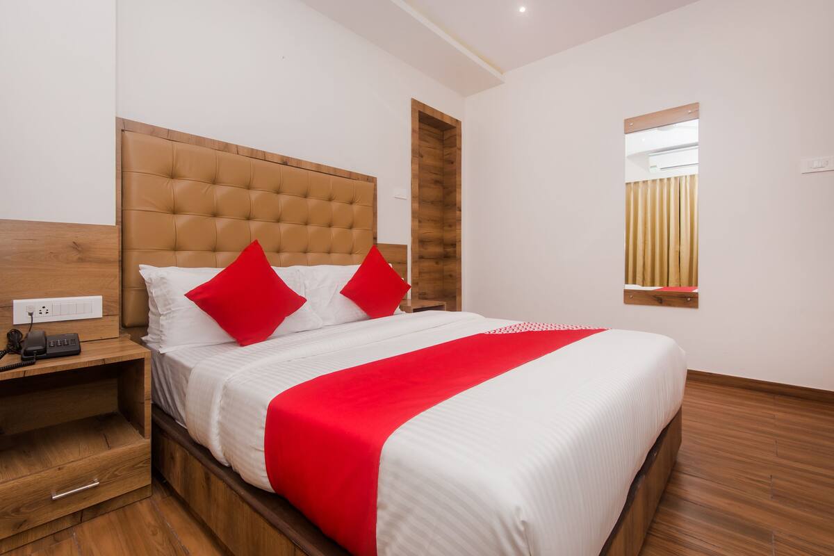 A neatly made bed with a red and white bedspread, a wooden headboard, and a bedside table with a phone and a lamp.