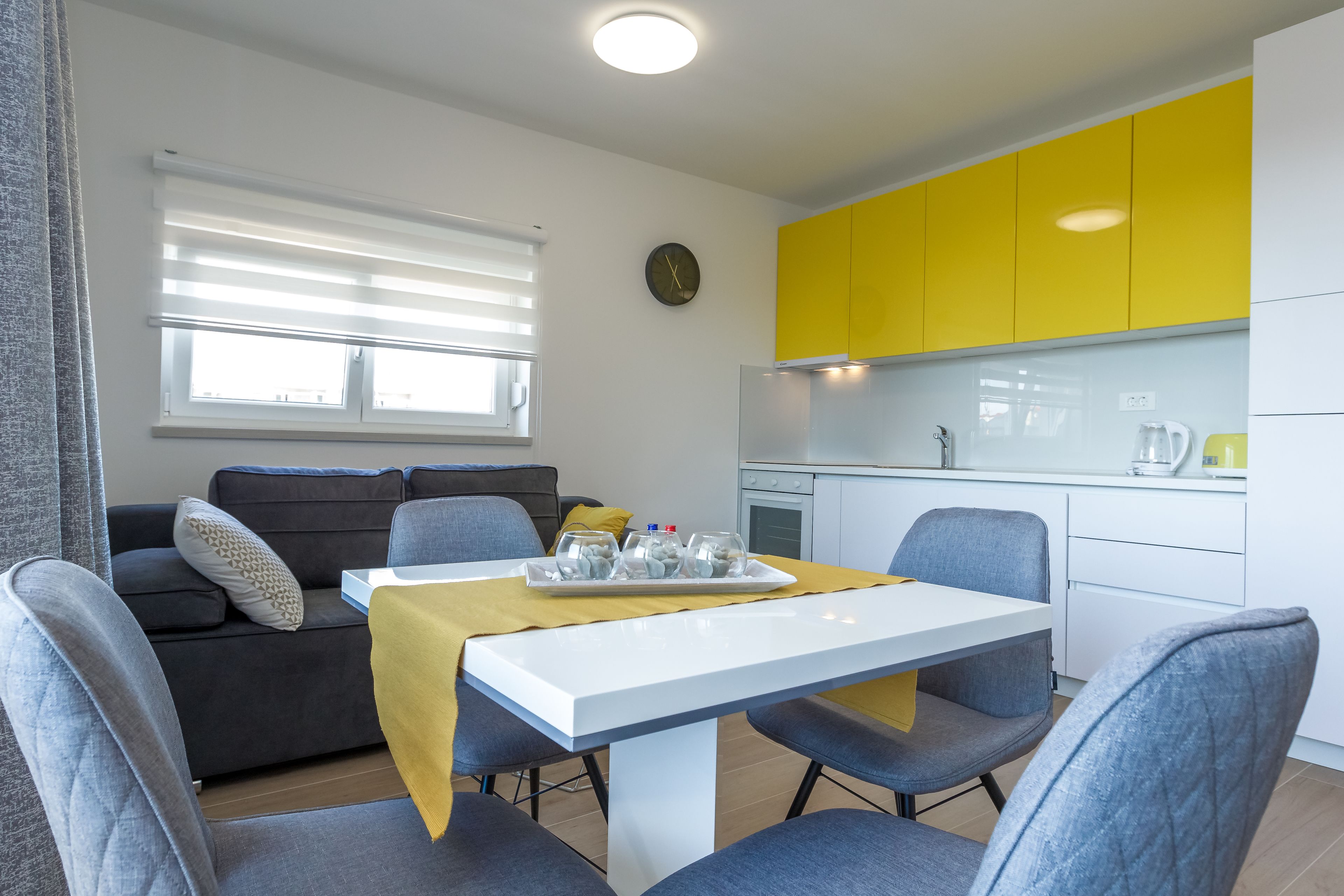 Un salon moderne avec un canapé, une table à manger et des chaises, ainsi qu’un coin cuisine doté de meubles jaunes.
