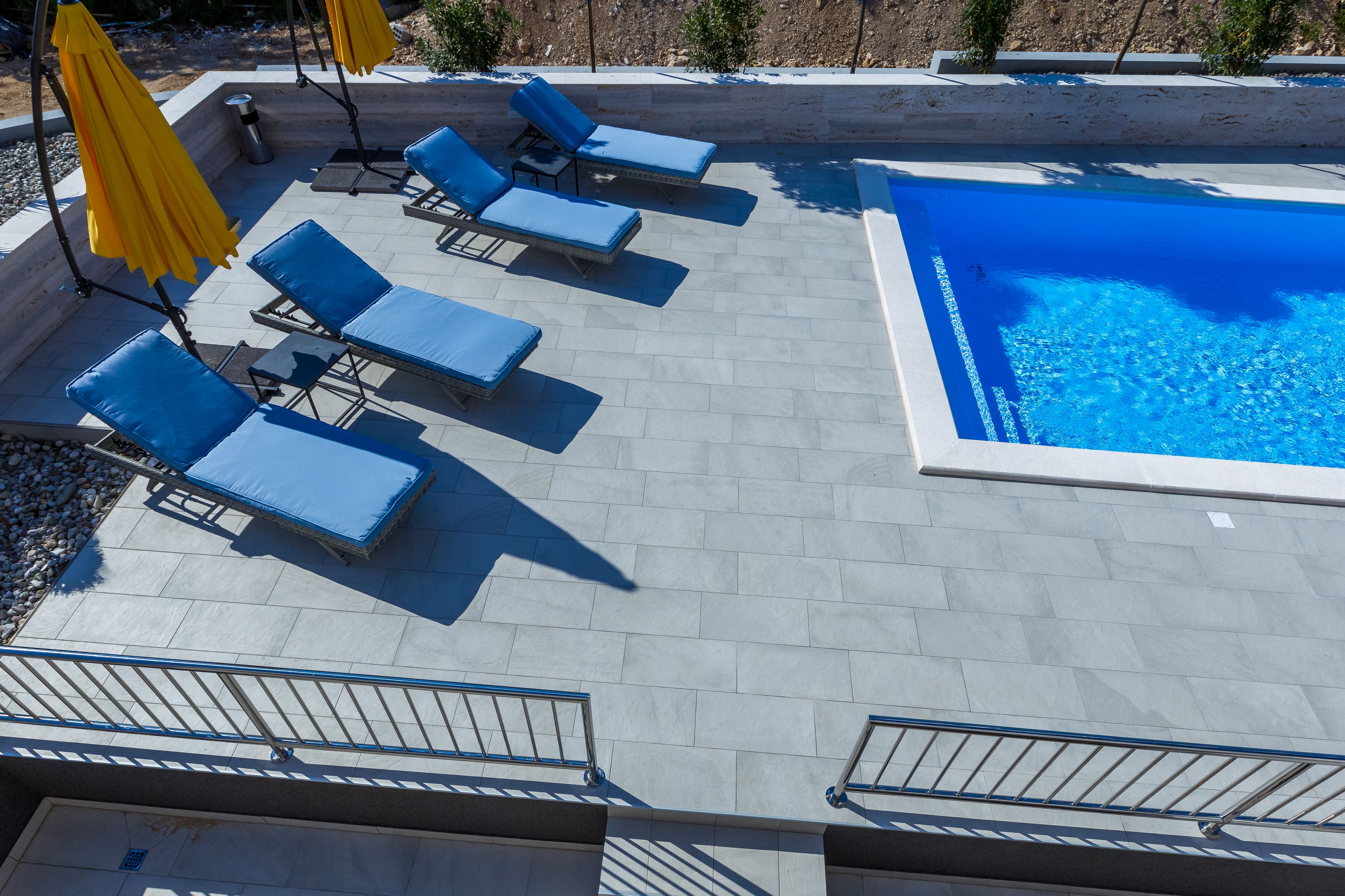 Zona de piscina con sillas reclinables azules y sombrillas amarillas.