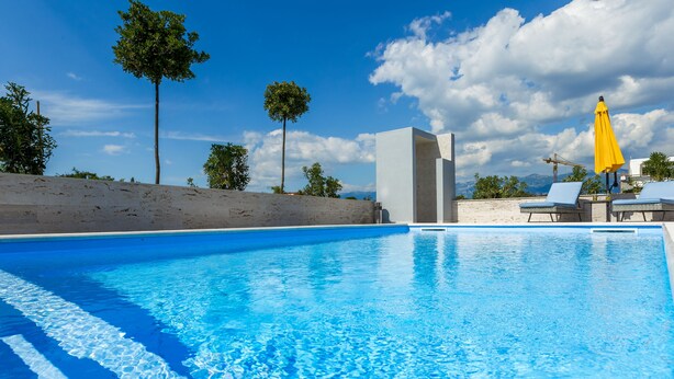 A clear blue pool with lounge chairs and a yellow umbrella, surrounded by trees and a view of mountains. - Apartments & Rooms Villa Casia (Novalja)