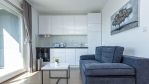 A modern living room with a grey sofa, a small coffee table, and a kitchen area with white cabinets and appliances. - Apartments & Rooms Villa Casia (Novalja)