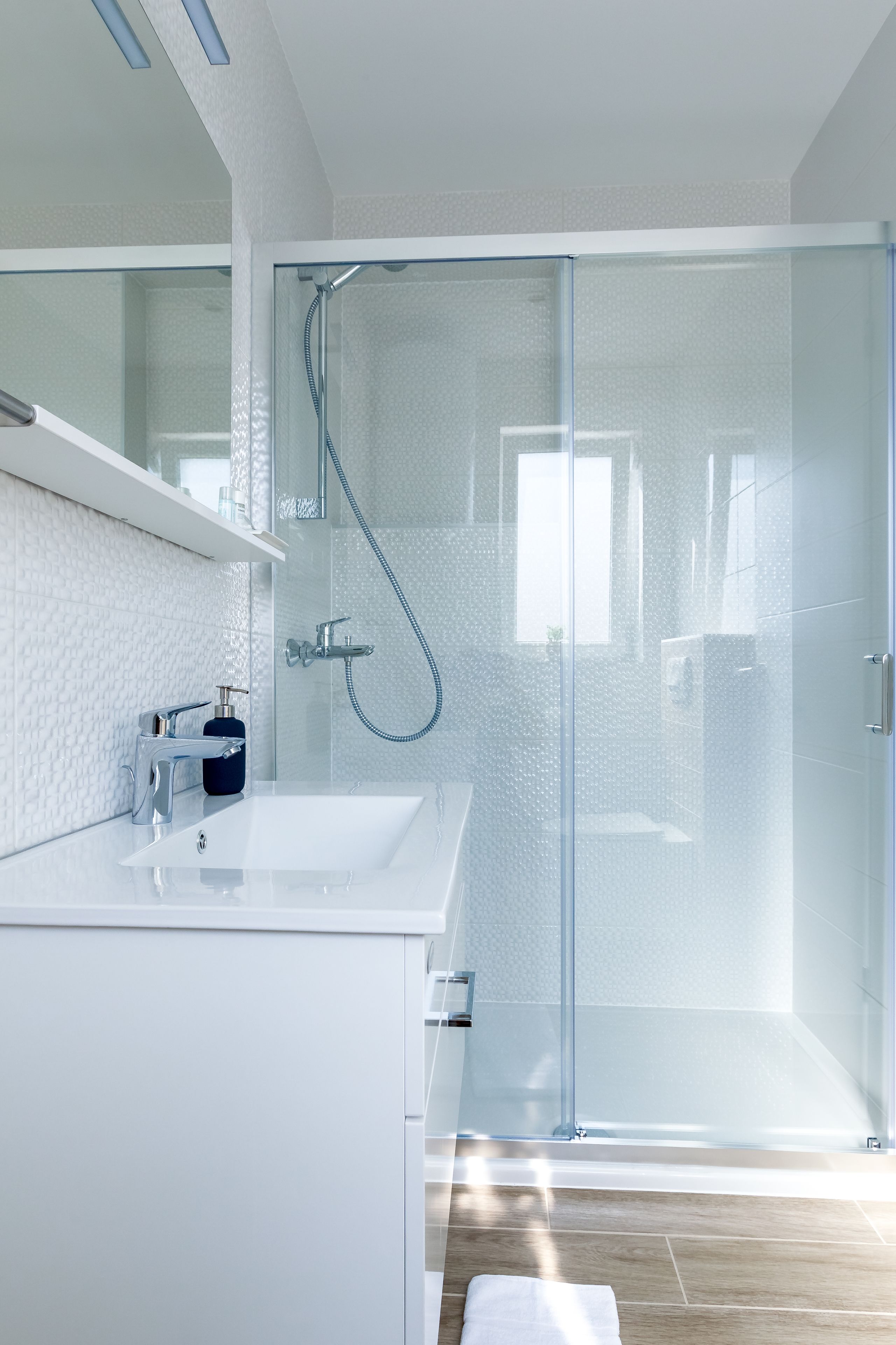 A modern bathroom with a glass shower enclosure, a white sink, and a wooden floor.