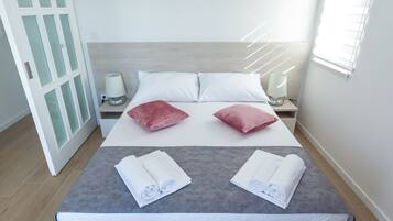 A neatly made bed with white and red pillows, two bedside lamps, and a window with blinds.