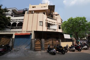 A multi-story building with a gated entrance, parked scooters, and a tree in the foreground. - CAPITAL O 15141 Townvilla Guest House (Hyderabad)