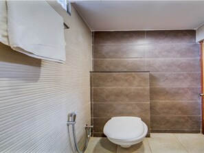 A bathroom with a toilet, a shower area, and a towel hanging on the wall. - CAPITAL O 15141 Townvilla Guest House (Hyderabad)