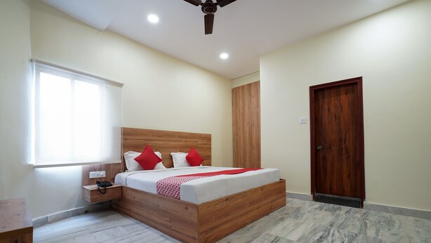 A bedroom with a wooden bed, a nightstand, a wooden wardrobe, a door, and a window with blinds. - CAPITAL O 15141 Townvilla Guest House (Hyderabad)