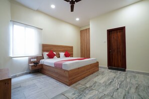 A bedroom with a wooden bed, a nightstand, a wooden wardrobe, a door, and a window with blinds. - CAPITAL O 15141 Townvilla Guest House (Hyderabad)