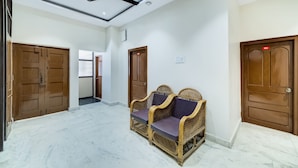 A spacious hallway with wooden doors, a ceiling fan, and a seating area with wicker furniture. - CAPITAL O 15141 Townvilla Guest House (Hyderabad)