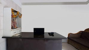 A modern room with a black table, a laptop, a wicker sofa, and a white cabinet with a colorful painting. - CAPITAL O 15141 Townvilla Guest House (Hyderabad)