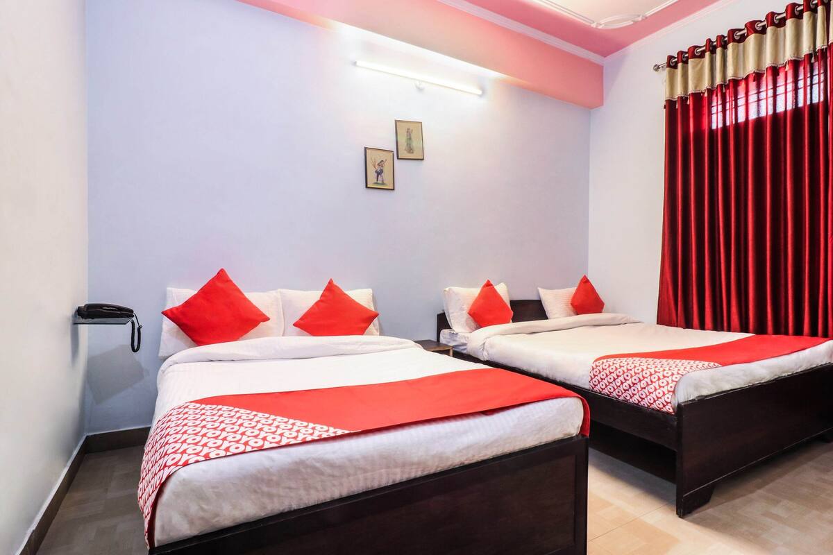 A hotel room with two beds, each with red and white bedding, a bedside table, a phone, and a wall-mounted light.