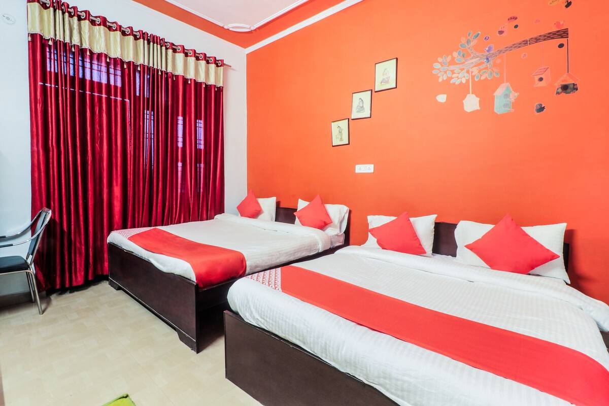 A hotel room with two beds, red and white bedding, a red curtain, and a wall with framed pictures.