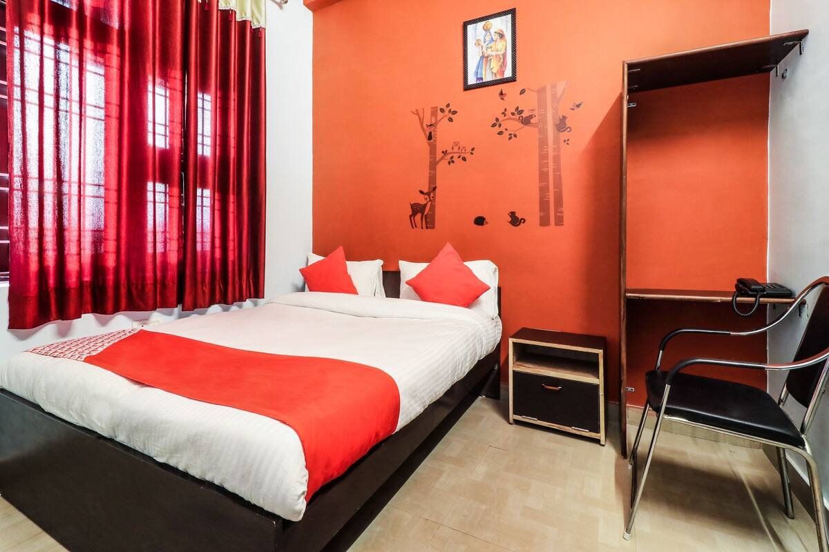 A bedroom with a bed, red curtains, a red wall, a small desk, and a chair.