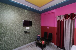 A room with a patterned green wall, a flat-screen TV mounted on the wall, a small table with a sign, two black chairs, and a red curtain. - OYO 18490 Hotel Jagannath International (Barakpur)