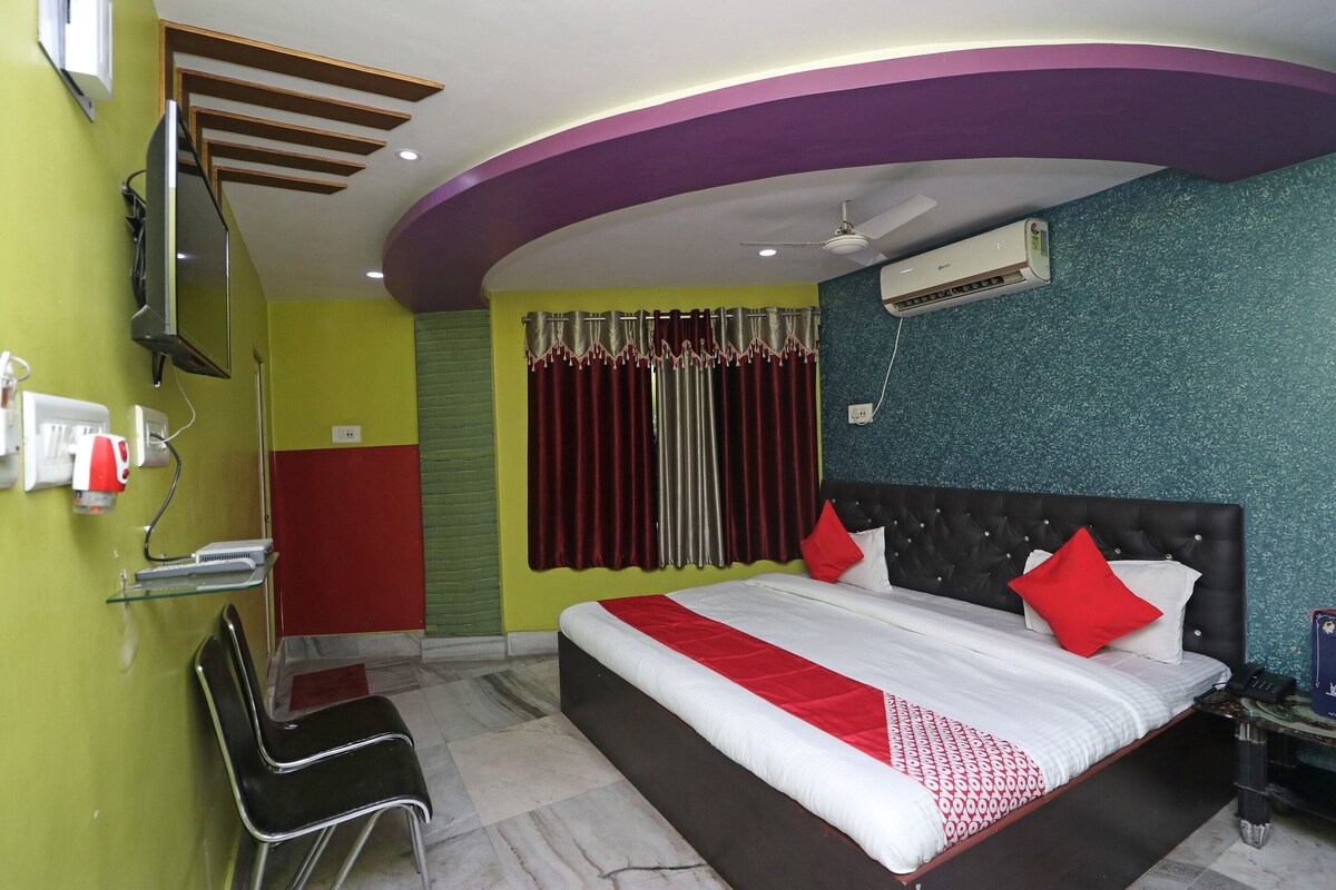 A hotel room with a bed, a chair, a TV, an air conditioner, and a window with curtains.
