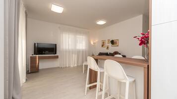 A modern living room with a flat-screen TV, a wooden dining table, white chairs, and a white sofa.
