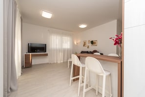 A modern living room with a flat-screen TV, a wooden dining table, white chairs, and a white sofa. - Apartments & Rooms Pool Villas Maris (Novalja)