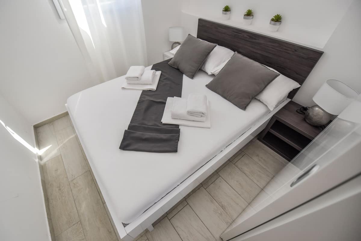 A modern hotel room with a neatly made bed, a bedside table with a lamp, and a small potted plant on the nightstand.