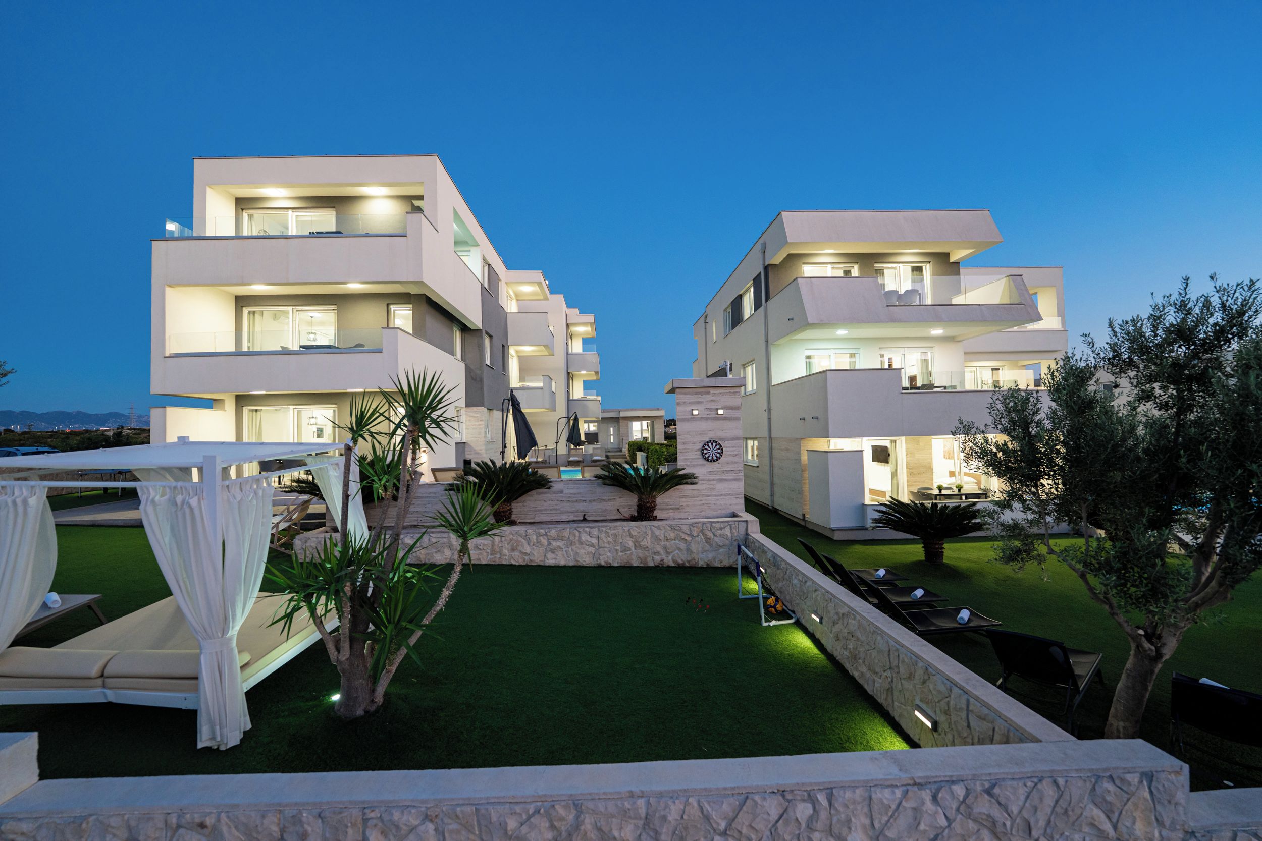 A modern multi-story hotel with a pool area, outdoor seating, and a well-maintained lawn.