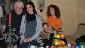 Un grupo de personas sentadas en una sala con una mesa que muestra frutas y un candelabro.