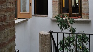 Un patio con un muro de ladrillo, una puerta de madera, una ventana con espejo y un pequeño balcón con una planta.