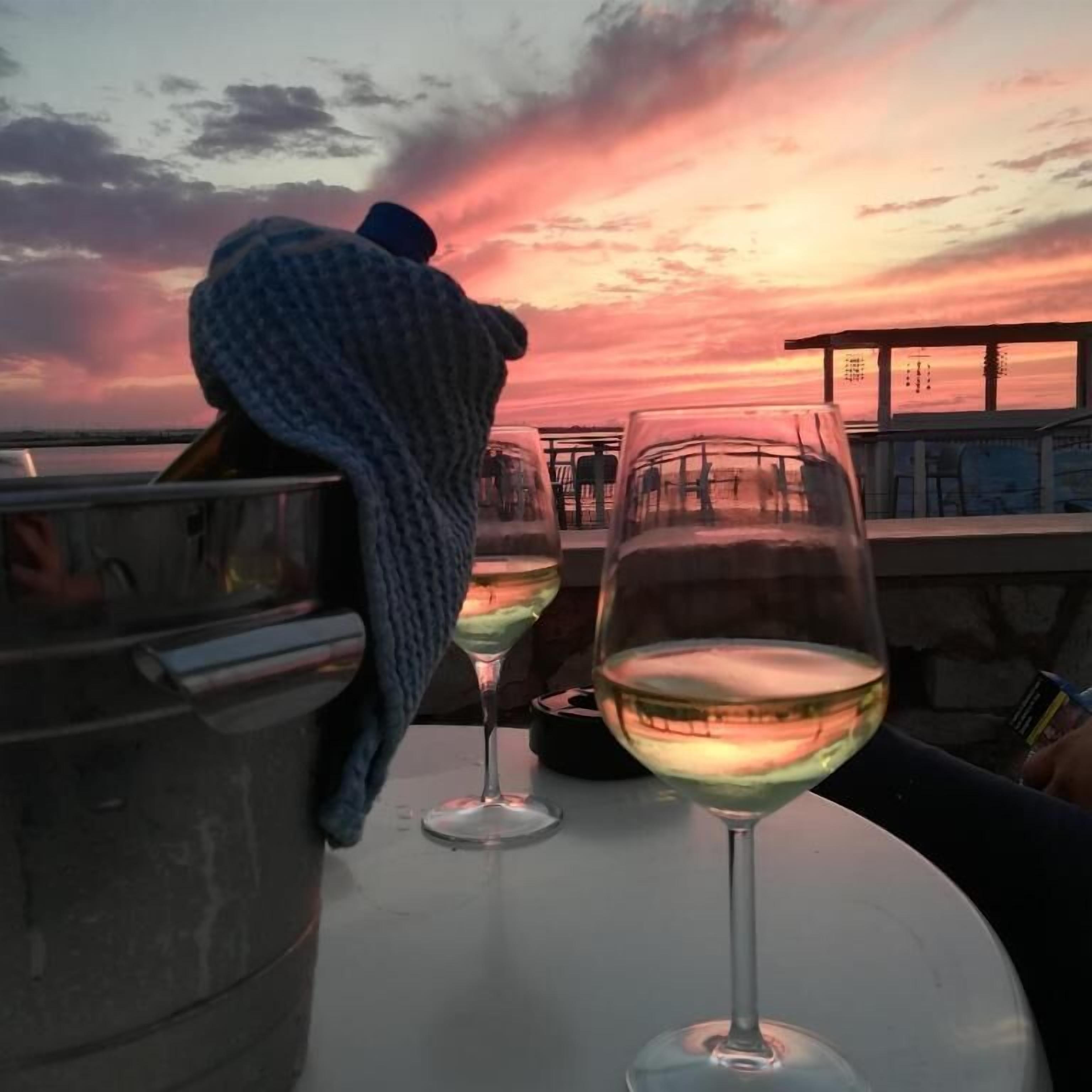 A table with two wine glasses and a metal container, set against a sunset backdrop.