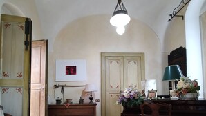 Una habitación con un piano de madera, un tapete verde estampado, una silla de madera, un sofá y una lámpara fijada a la pared.