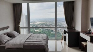 A modern bedroom with a large bed, a desk, and a view of a cityscape through large windows.