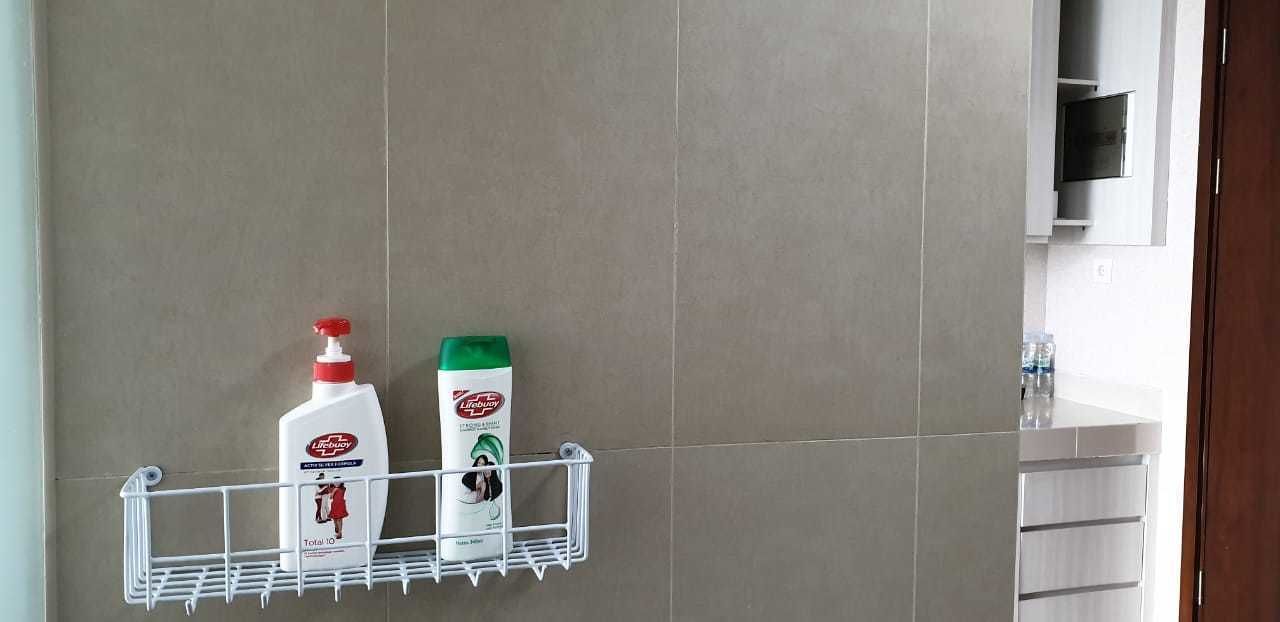 A bathroom with a wall-mounted shelf holding two bottles of lotion and a bottle of shampoo.
