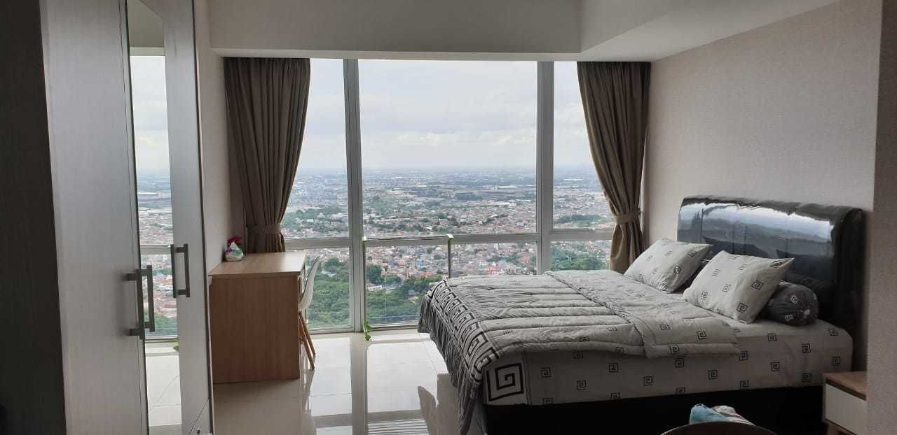 Ein Schlafzimmer mit einem großen Bett, einem Nachttisch und Blick auf eine Stadtlandschaft durch ein großes Fenster.