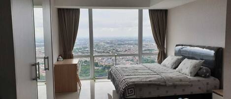 Ein Schlafzimmer mit einem großen Bett, einem Nachttisch und Blick auf eine Stadtlandschaft durch ein großes Fenster.