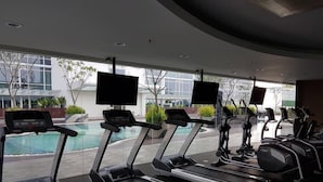 A gym with treadmills and stationary bikes, a pool, and large windows offering a view of the outside.