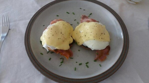 A plate with two poached eggs topped with hollandaise sauce and slices of ham, garnished with chives.