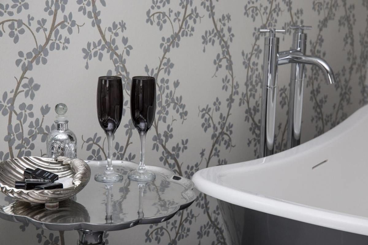A bathroom with a bathtub, a glass basin with two glasses, and a bottle of perfume on a tray.