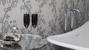 A bathroom with a bathtub, a glass basin with two glasses, and a bottle of perfume on a tray.