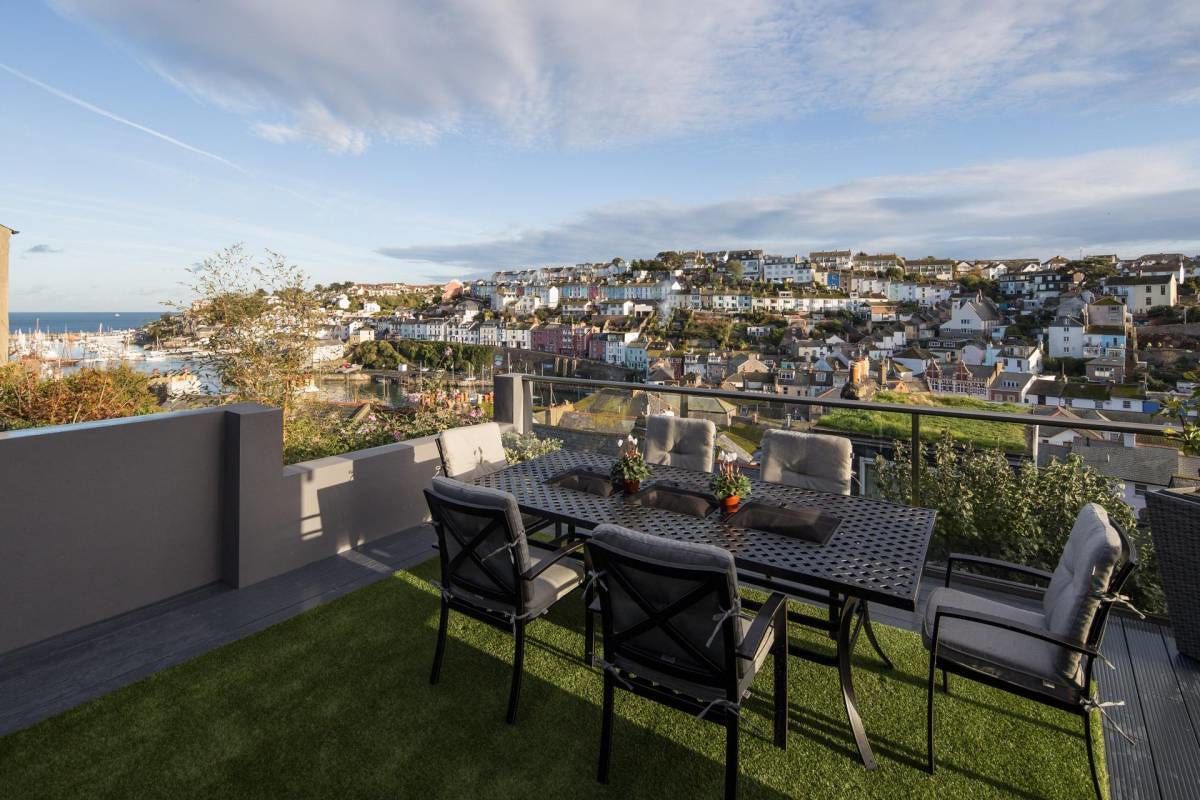 A terrace with a table and chairs, overlooking a coastal town.