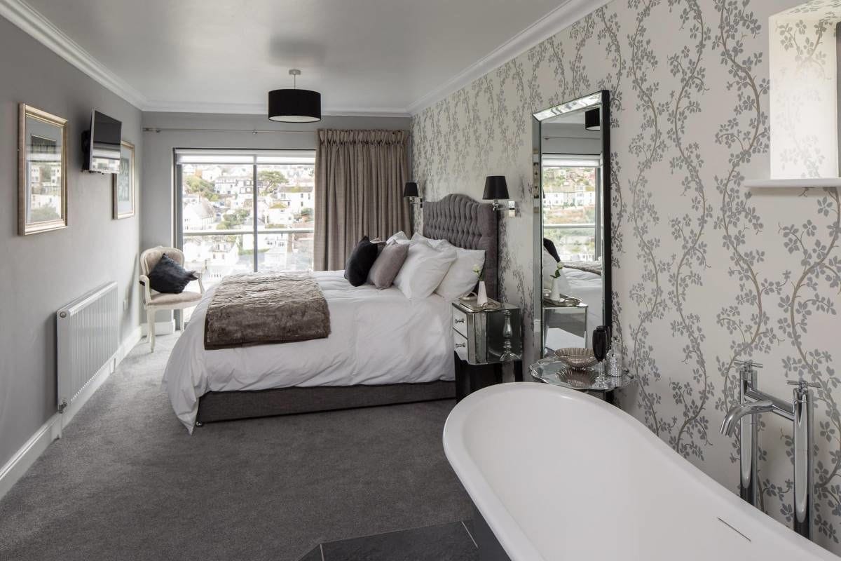 A bedroom with a large bed, a sitting area, and a bathroom with a bathtub.