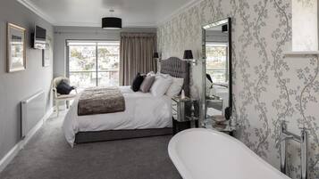A bedroom with a large bed, a sitting area, and a bathroom with a bathtub.