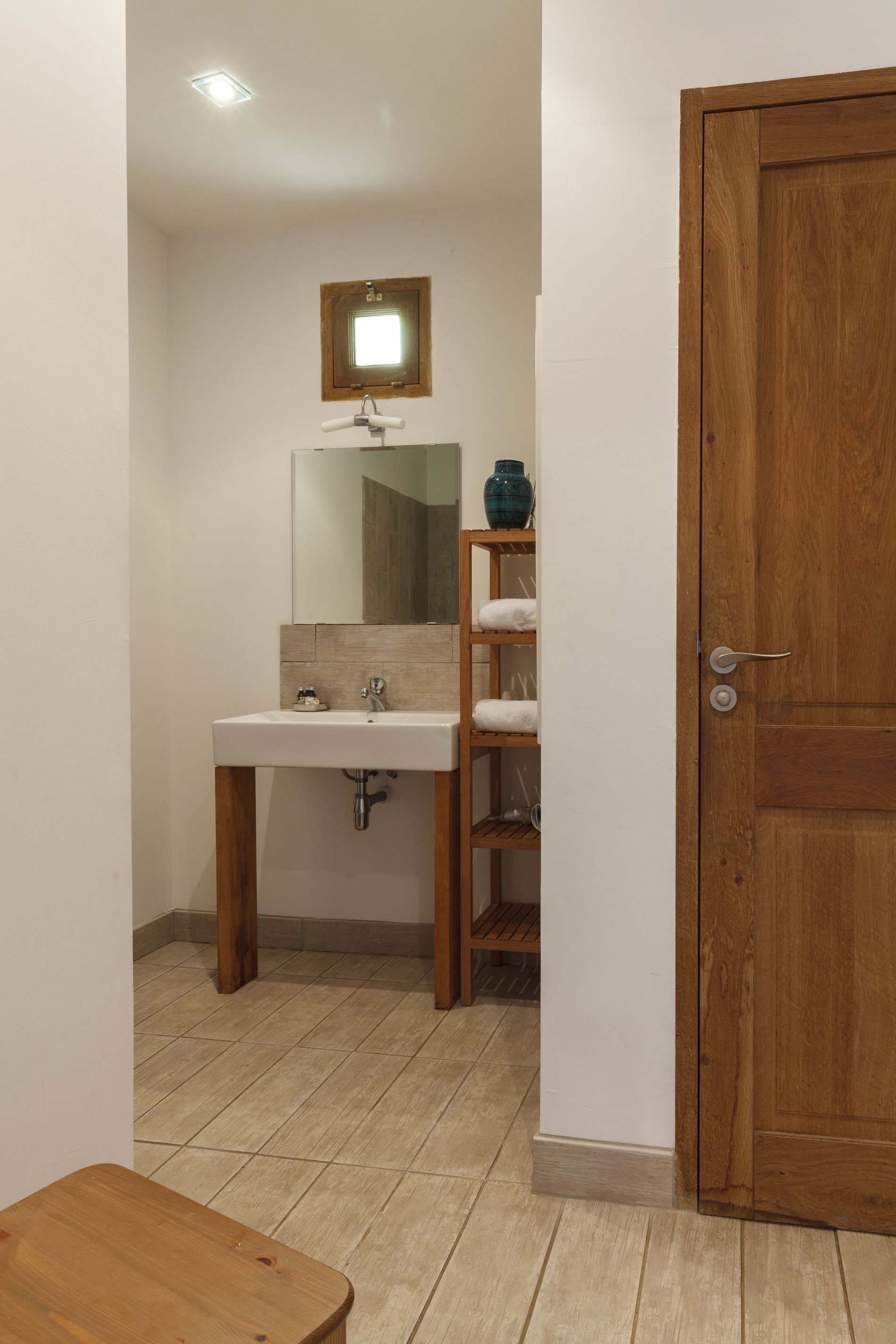Een badkamer met een houten wastafelmeubel, een wastafel, een spiegel en een plank met handdoeken.