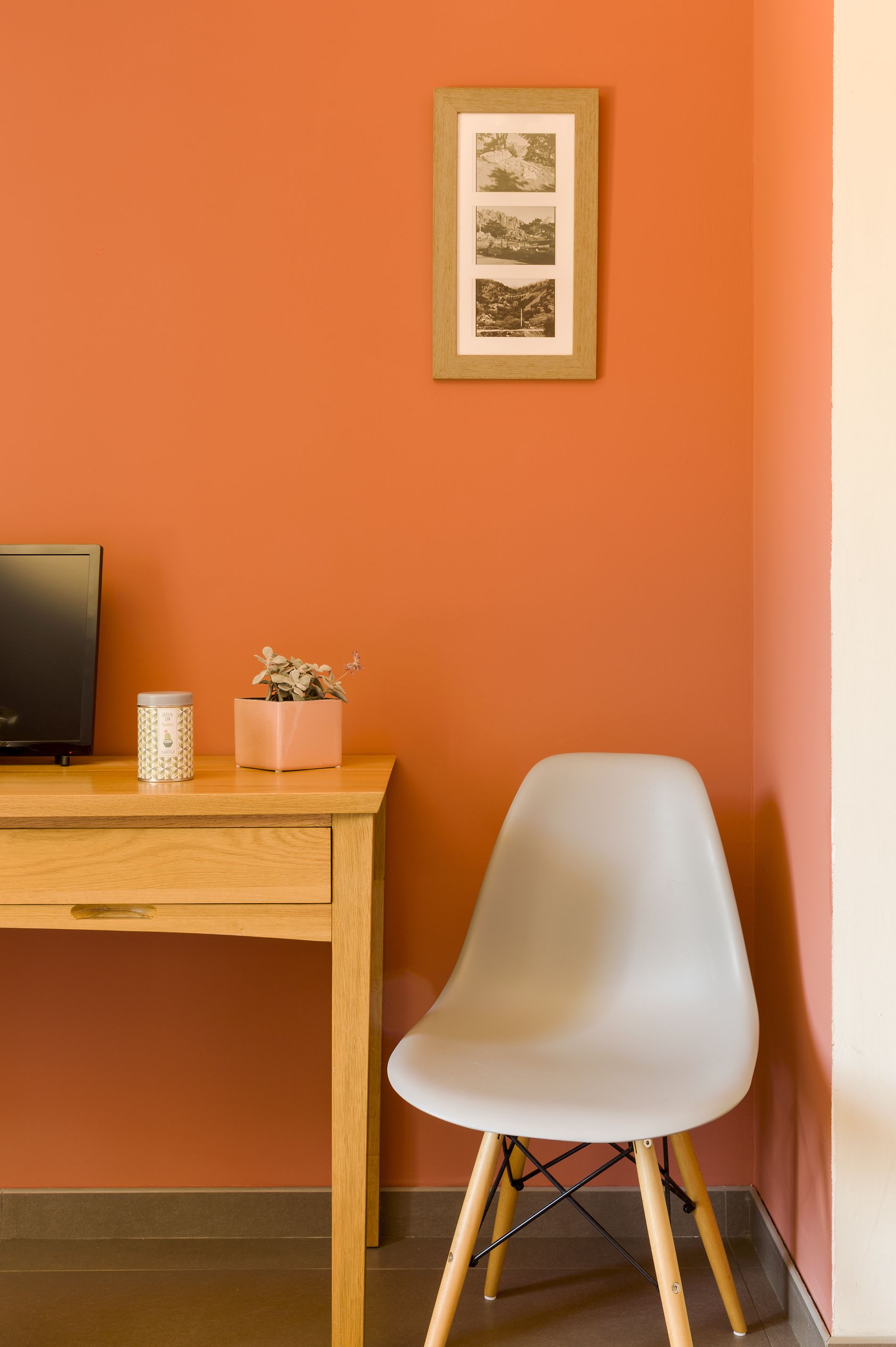 Een houten bureau met een witte stoel, een lijst met foto, een kleine pot met plant en een bakje op het bureau.