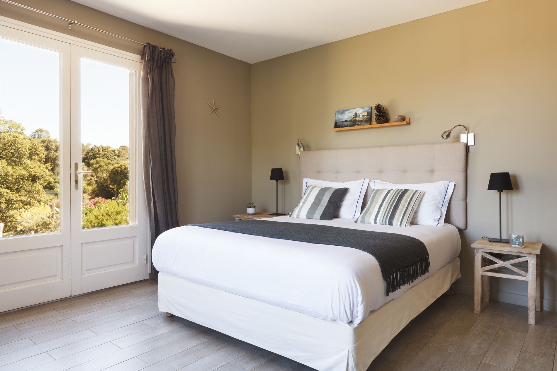 A bedroom with a large bed, two bedside tables, a nightstand, a window with curtains, and a starfish decoration on the wall.