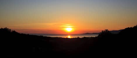 A sunset over a body of water with silhouettes of hills and trees.
